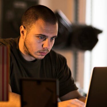 Man wearing black t-shirt working on his laptop.